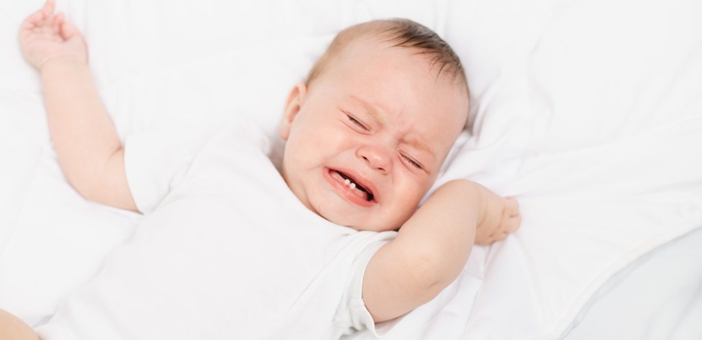 طفل رضيع يبكي ويمسك بيده طرف غطاء السرير