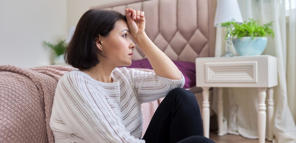 امرأة حزينة تجلس على الأرض بجانب السرير وتضع يدها على رأسها