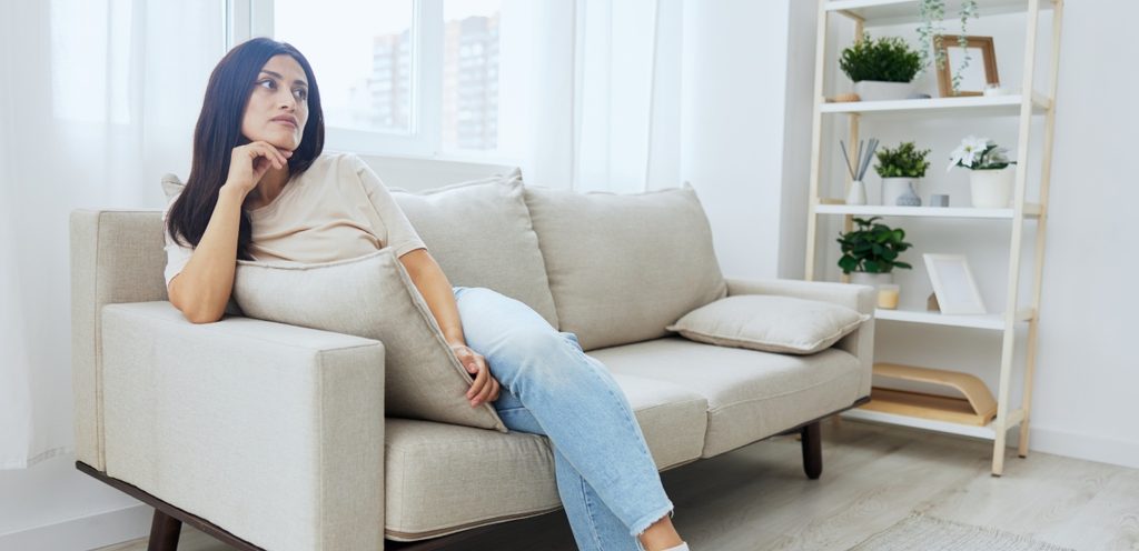 امرأة تجلس على الكنبة وتضع يدها تحت ذقنها وتنظر لأعلى