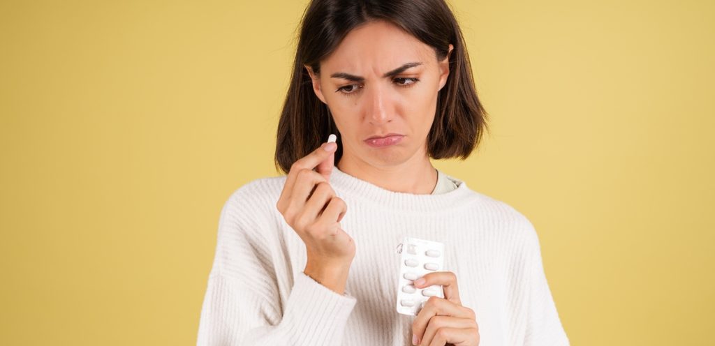 امرأة حزينة تمسك ظرف من الدواء في يدها وحبّة منه في يدها الأخرى وتنظر إليها