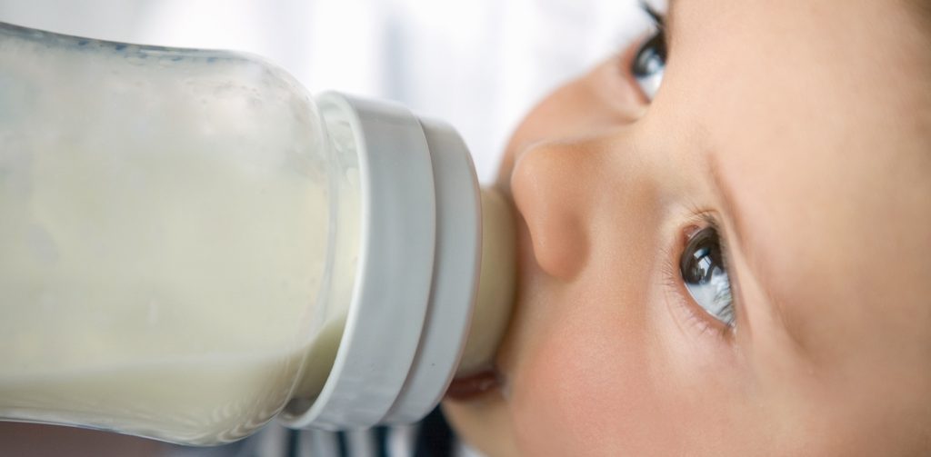 طفل رضيع يرضع زجاجة حليب وينظر لأعلى