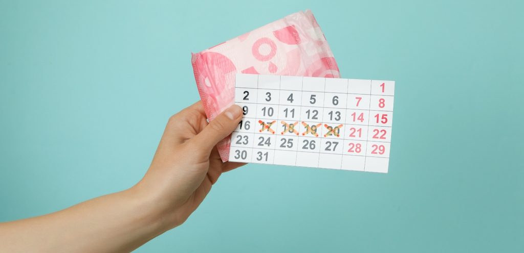 يد امرأة تمسك فوطة صحية وورقة عليها تواريخ