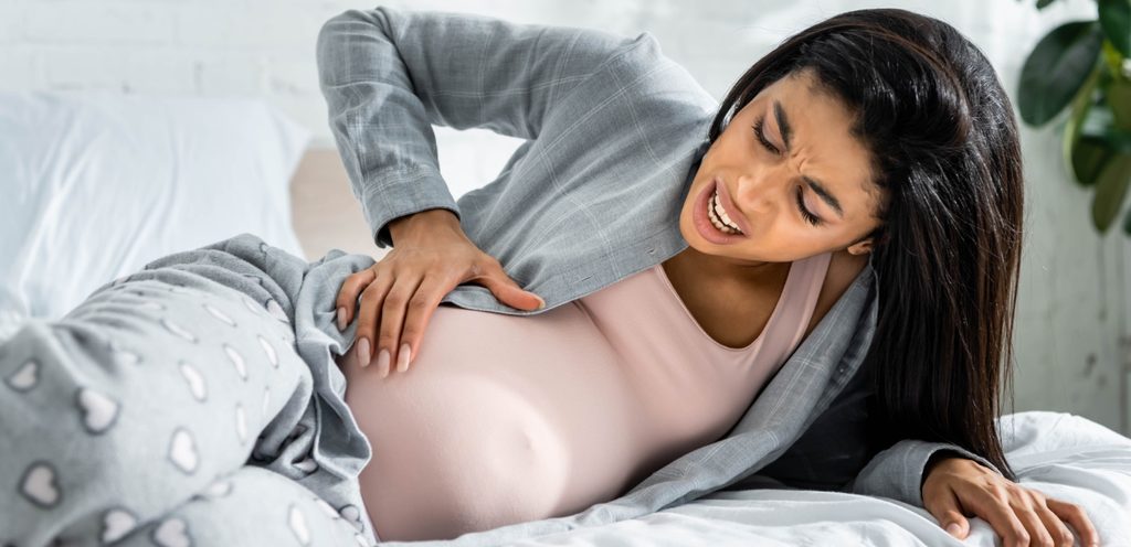 امرأة حامل مستلقية تشعر بالألم وتضع يدها على بطنها