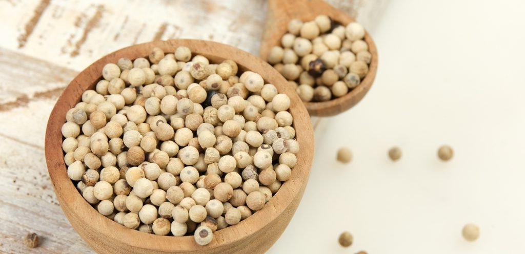 كاسة خشبيّة مع ملعقة خشبيّة يحتويان حبوب الفلفل الأبيض