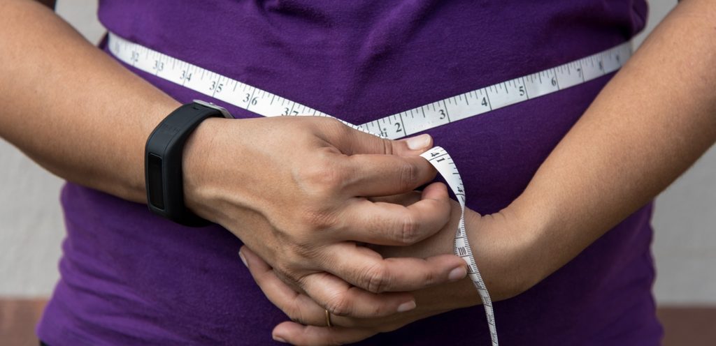 امرأة تلف شريط القياس حول خصرها وتمسكه بيديها