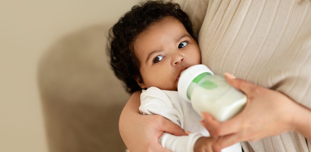 طفل رضيع تحمله أمّه ويرضع زجاجة حليب