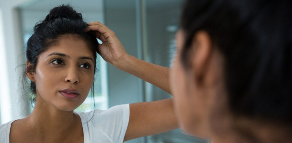 امرأة تنظر إلى المرآة وتضع يدها على رأسها