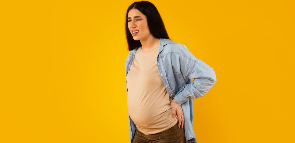 امرأة حامل تشعر بالألم وتضع يديها خلف ظهرها