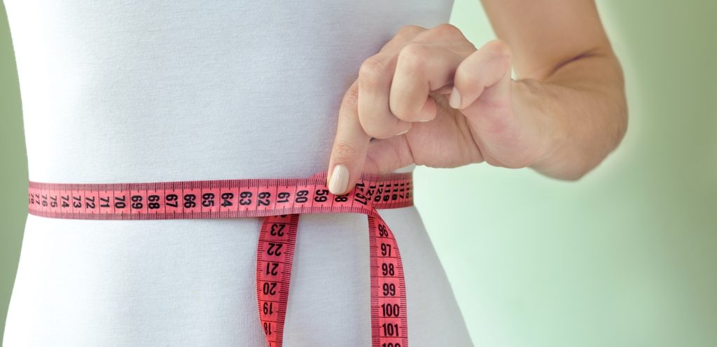 امرأة تلف شريط القياس حول خصرها وتجمع طرفيه بإصبعها