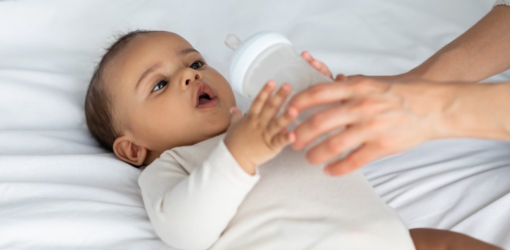 طفل رضيع مستلقِ على السرير يستعدّ لتناول الحليب ووالدته بجانبه