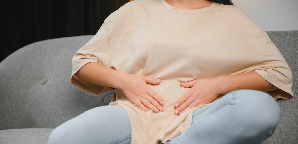 امرأة تجلس على الكنبة وتضع يديها على بطنها
