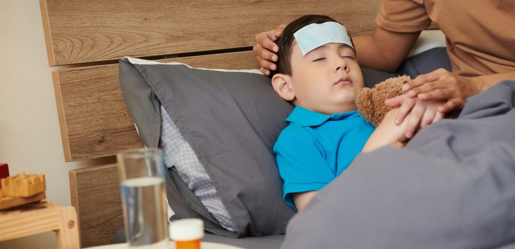 طفل نائم في السرير على رأسه قطعة قماش لخفض الحرارة  وبجانبه والدته