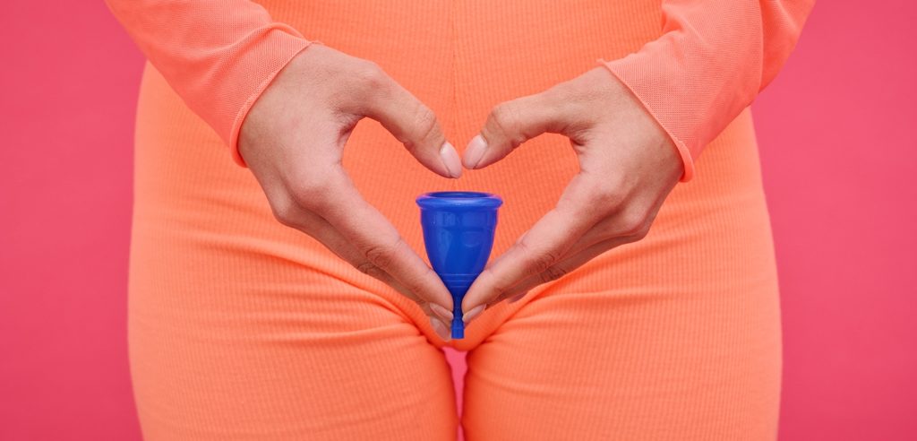 امرأة تمسك كوب الحيض بين يديها على شكل قلب
