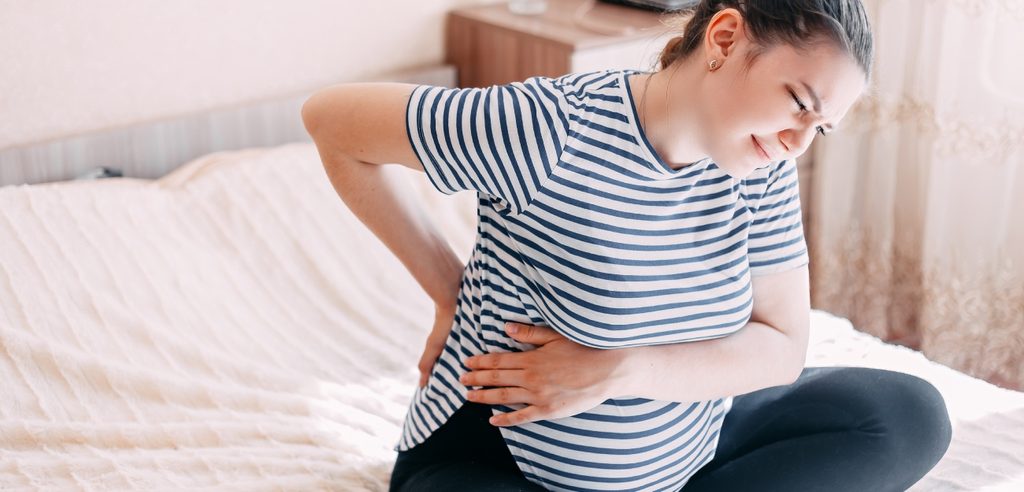 امرأة حامل تضع يديها على بطنها وظهرها وتشعر بالألم