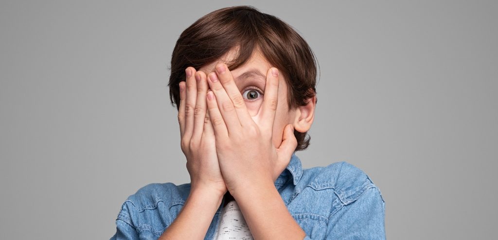 طفل يضع يديها على وجهه وبيرز عينه من بين أصابعه