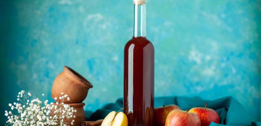 زجاجة من خلّ التفاح وبجانبها ثمار من التفاح الكاملة والمقطّعة