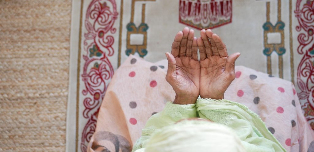 امرأة تجلس على سجادة الصلاة وترفع يديها للدعاء