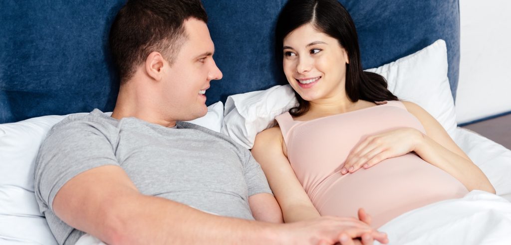 امرأة حامل سعيدة مستلقية بجانب زوجها على السرير