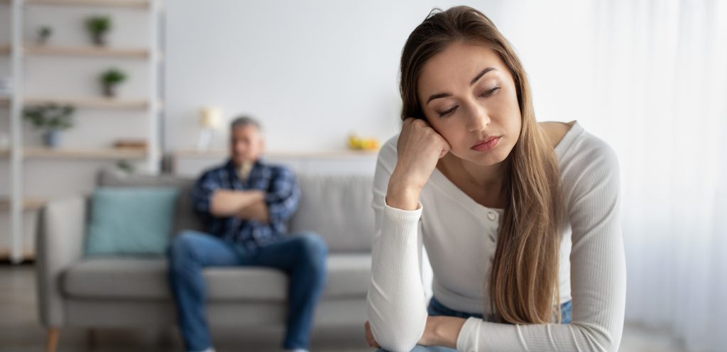 امرأة حزينة تجلس وحدها وزوجها خلفها