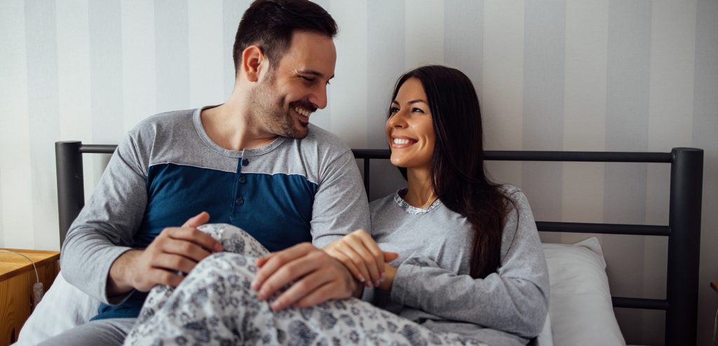 زوجان مستلقيان في السرير ينظران إلى بعضهما البعض بسعادة