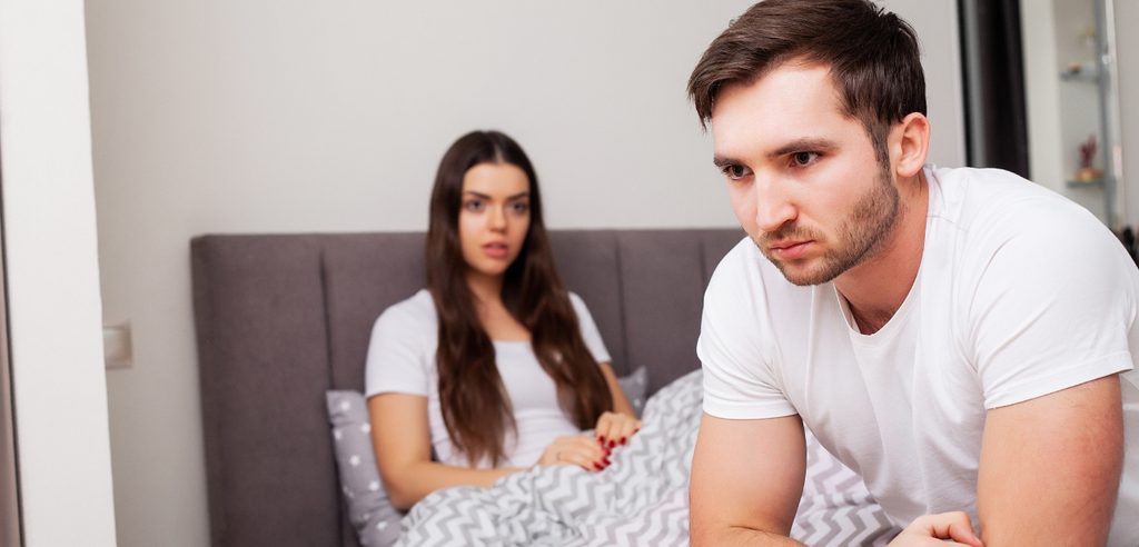 امرأة حزينة في السرير وزوجها يجلس أمامها غاضبًأ