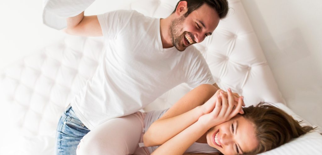 رجل يلعب مع زوجته بالمخدّة على السرير