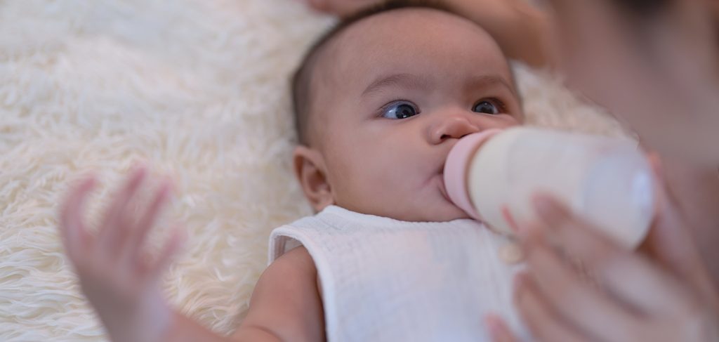 طفل رضيع ينظر إلى والدته وهي تمسك له زجاجة الحليب التي يشرب منها