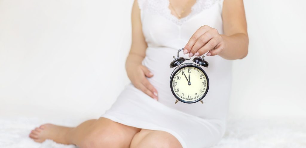 امرأة حامل تضع يدها على بطنها وتمسك ساعة