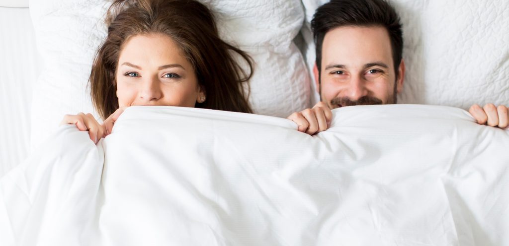 زوجان يبرزان رأسهما من تحت غطاء السرير