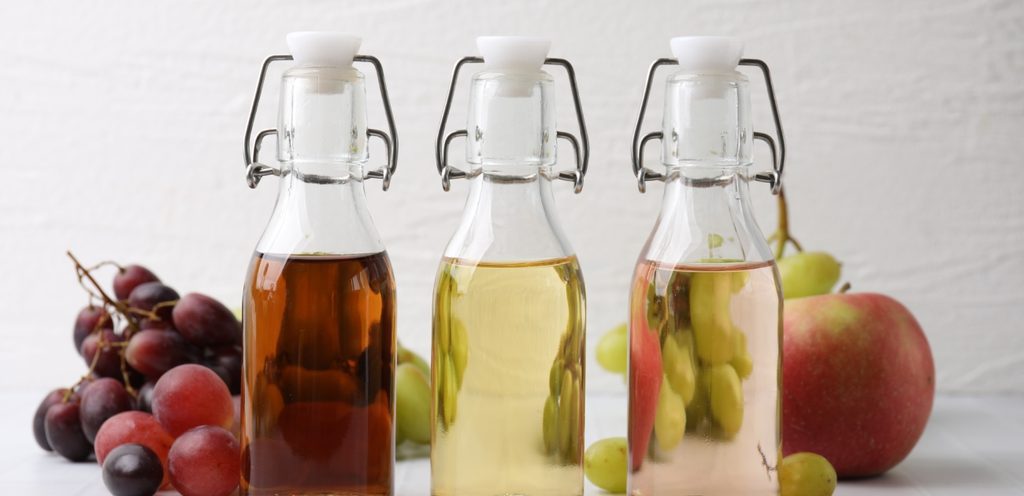 ثلاثة زجاجات من الخل وخلفها عنب وتفّاح