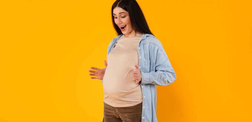 امرأة حامل تنظر إلى بطنها بسعادة وتفتح يديها