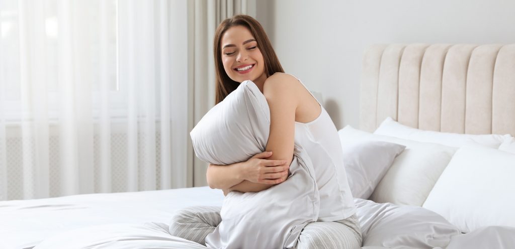 امرأة سعيدة تجلس في السرير وتحتضن وسادتها