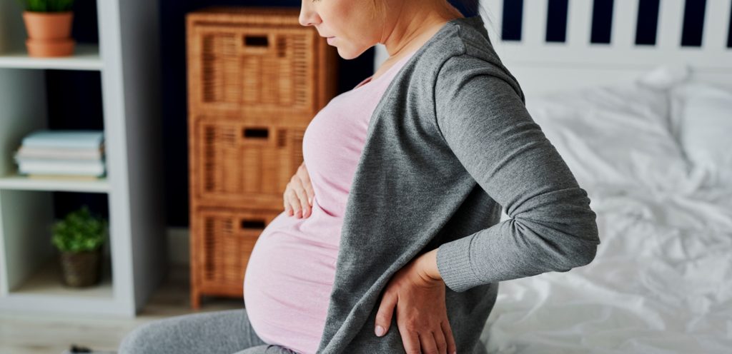 امرأة حامل تجلس وتضع يدها على بطنها واليد الأخرى خلف ظهرها