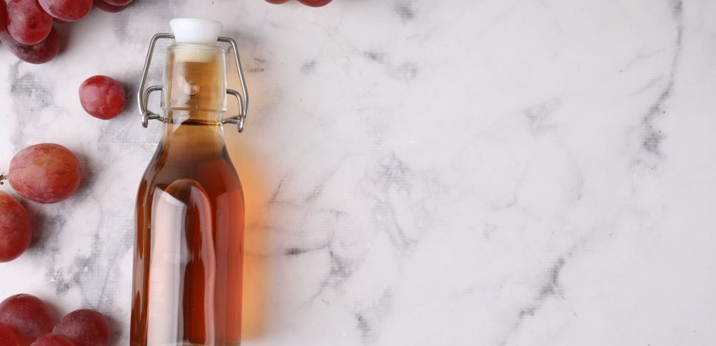زجاجة من الخل وبجانبها حبّات من العنب الأحمر
