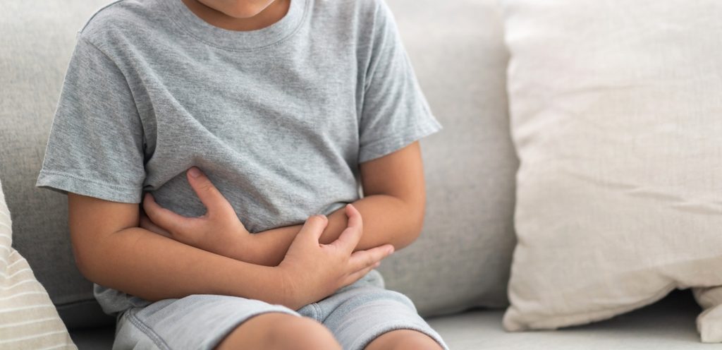 طفل يجلس على الكنبة ويضع يديه على بطنه