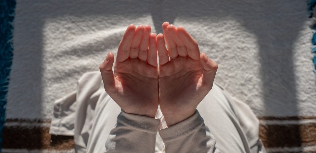 امرأة تجلس على الأرض وترفع يديها للدعاء