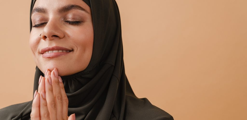 امرأة مسلمة مبتسمة تجمع كفَّي يديها للدعاء