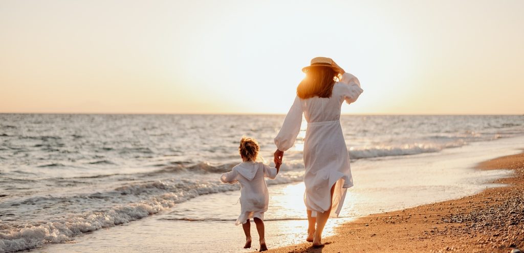 أمّ تمسك يد طفلها ويتمشيّان على شاطئ البحر