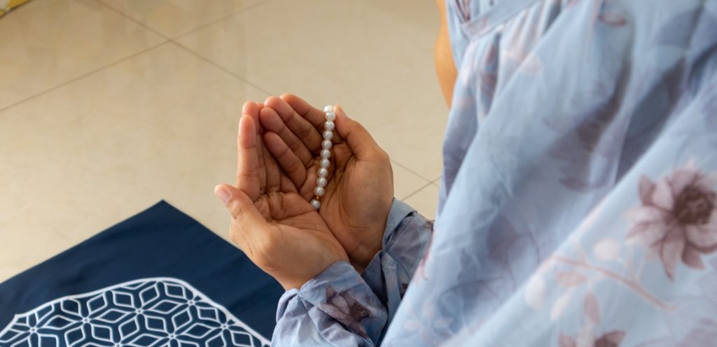امرأة مسلمة ترفع يديها للدعاء وتمسك مسبحة