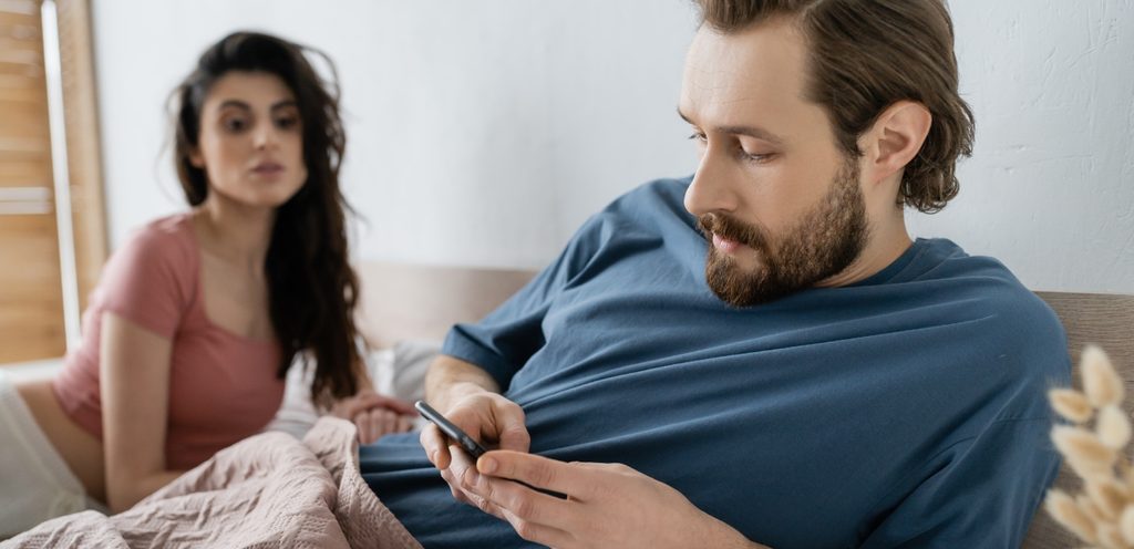 رجل يمسك هاتفه وزوجته تراقبه
