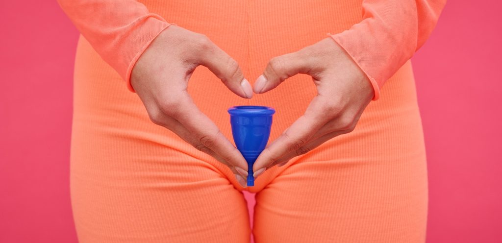 امرأة تصنع شكل قلب بيديها وتمسك كوب الحيض