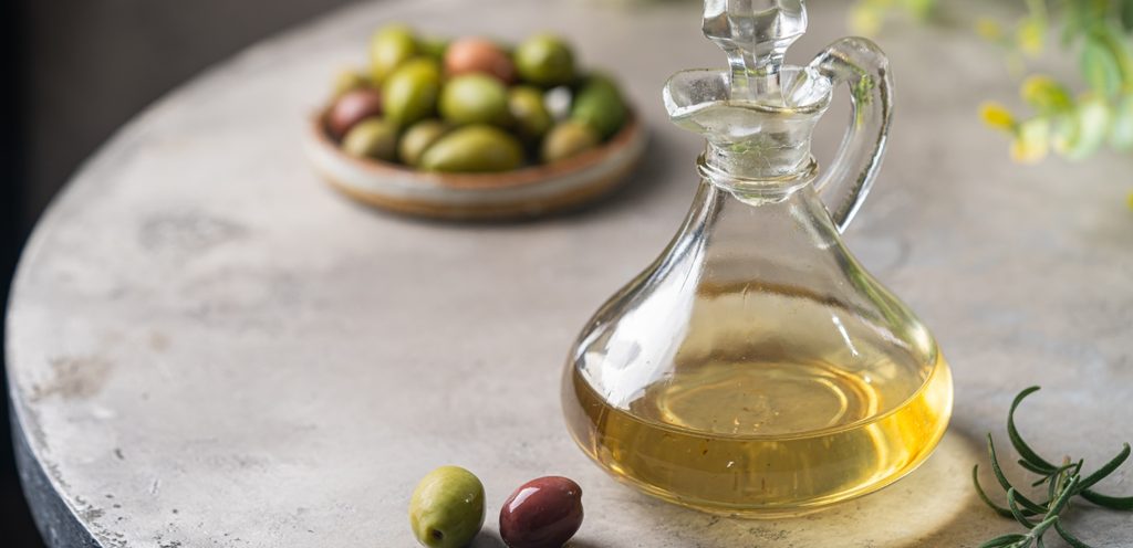 زجاجة من الزيت وخلفها طبق يحتوي حبوب الزيتون