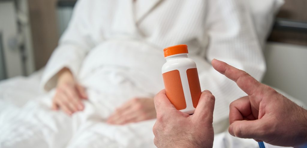 امرأة حامل تجلس في السرير وأمامها شخص يمسك علبة من الدواء