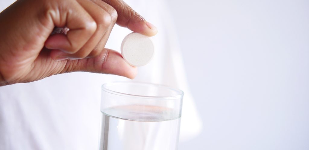 امرأة تمسك قرص فوار وتضعه في كأسٍ من الماء