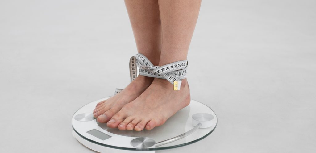 امرأة تقف على الميزان ويربط رجليها شريط قياس