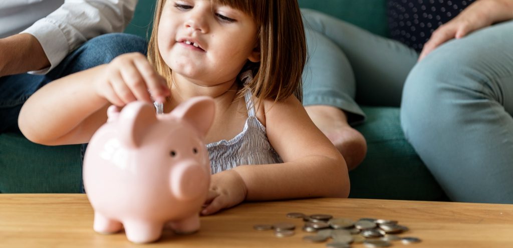 طفلة تضع نقود معدنيّة في صندوق الادّخار