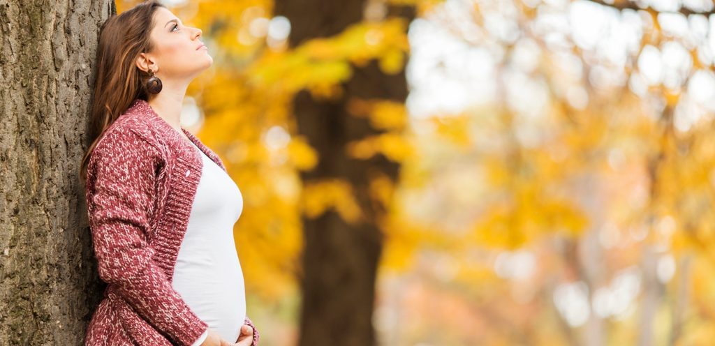امرأة حامل تنظر لأعلى وتستند على جذع شجرة