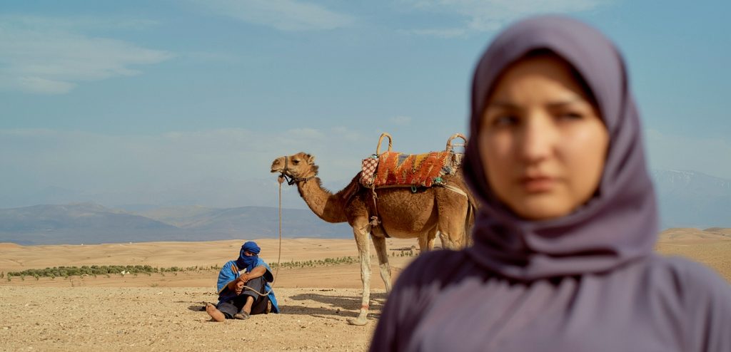 رجل يمسك حبل يربط به الجمل وأمامهما امرأة