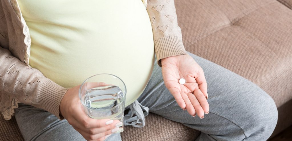 امرأة حامل تمسك كوبًا من الماء وحبوبًا من الدواء