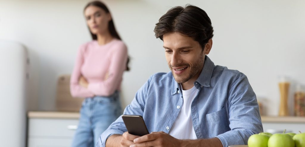 رجل يمسك هاتفه ويبتسم وامرأة خلفه تنظر إليه